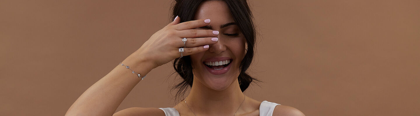 Woman laughing while showing diamond engagement rings, bracelet and necklace, bridal jewellery inspiration for modern proposals